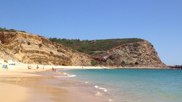 Une plage à l’eau turquoise et limpide, bordée d’un rivage sablonneux et de falaises rocheuses.