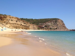 Une plage à l’eau turquoise et limpide, bordée d’un rivage sablonneux et de falaises rocheuses.