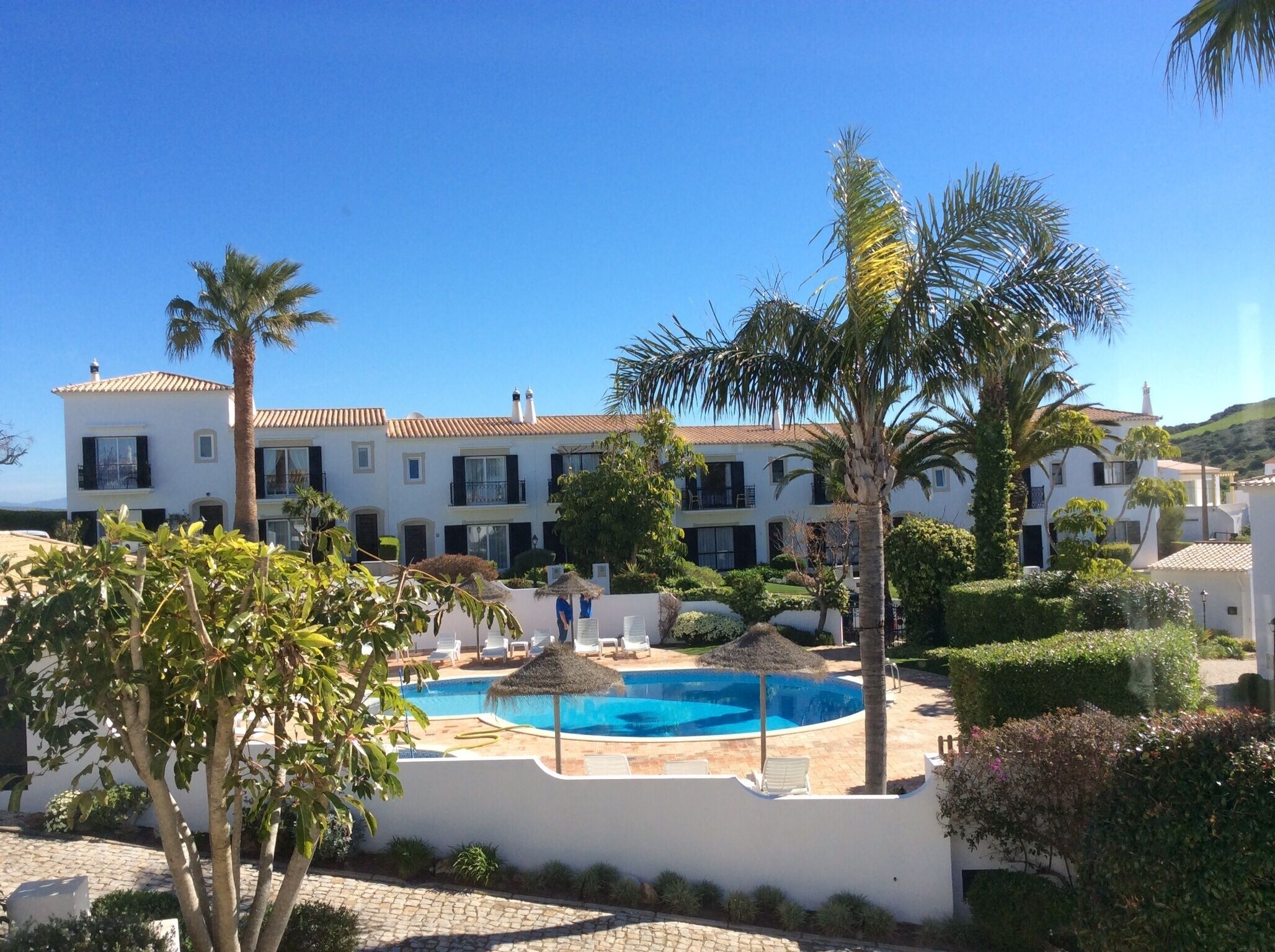 A resort with a swimming pool, palm trees, and a white building with multiple balconies.