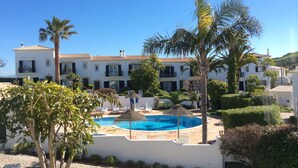 Un complexe hôtelier doté d’une piscine, de palmiers et d’un bâtiment blanc orné de nombreux balcons.
