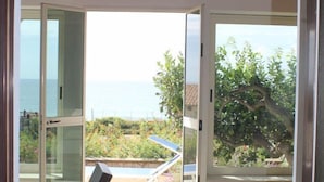 Una habitación con techo de madera, vista al mar, una silla de mimbre y un mantel a cuadros.