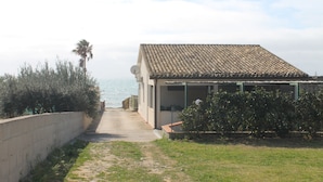 Una casa costera con techo de tejas, un camino empedrado que lleva a la entrada y vista al mar de fondo.