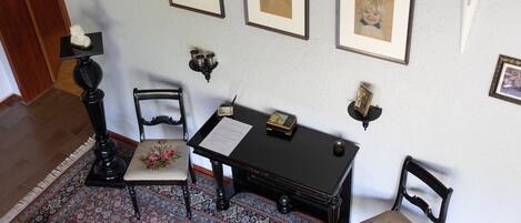 A room with a patterned rug, a desk with a lamp, chairs, and framed pictures on the wall.