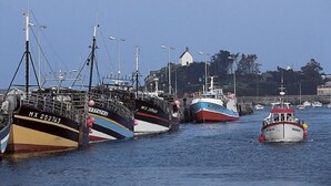 Ein Hafen mit mehreren vor Anker liegenden Booten, einem Leuchtturm und einem Gebäude mit Kuppel im Hintergrund.