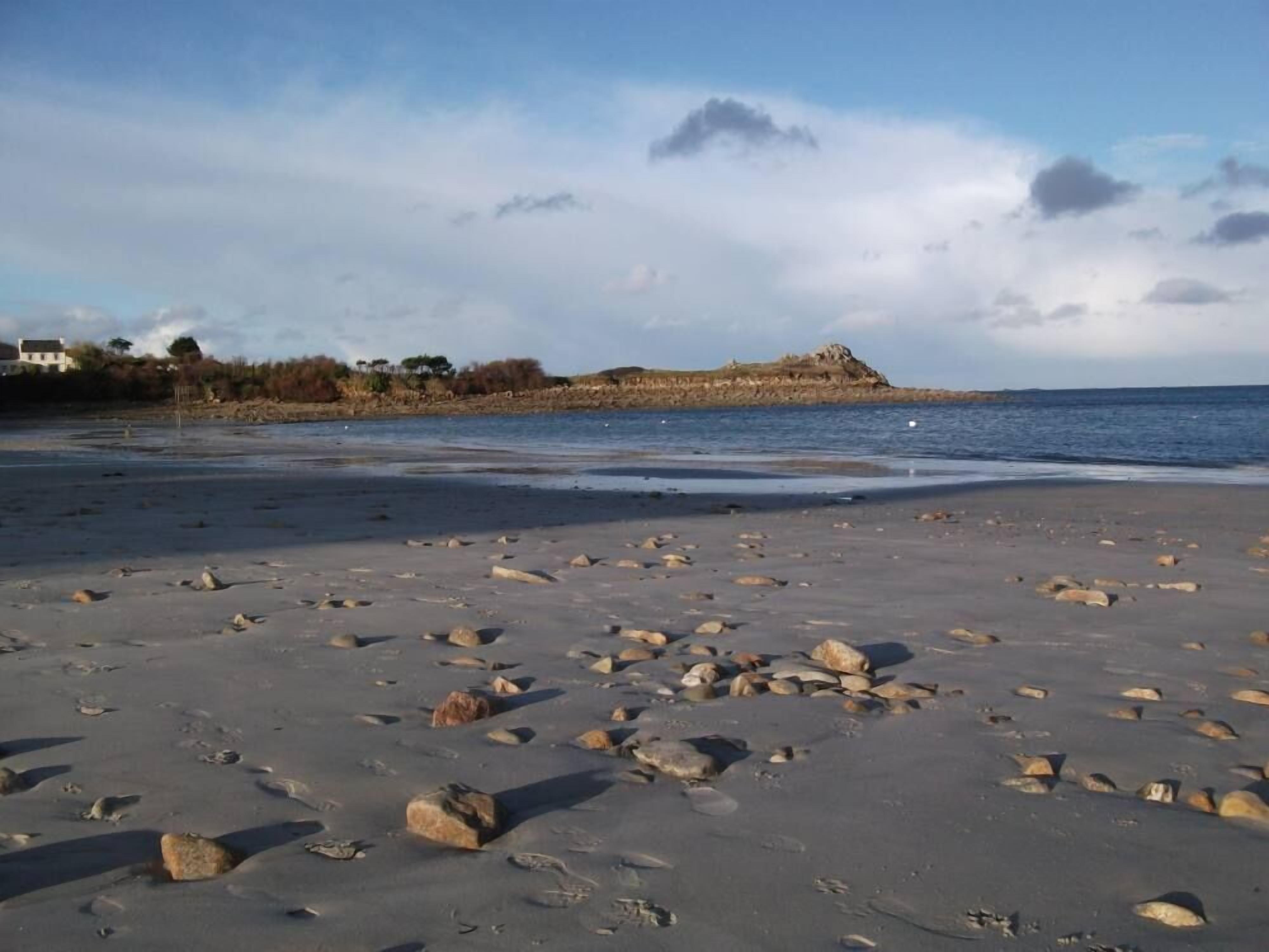 A beach with scattered rocks and a distant rocky outcrop.