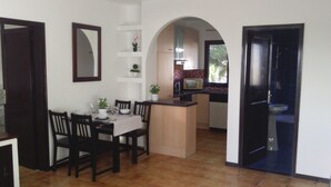 A dining area with a table set for four, a kitchen with a tiled backsplash, and an archway leading to another room.
