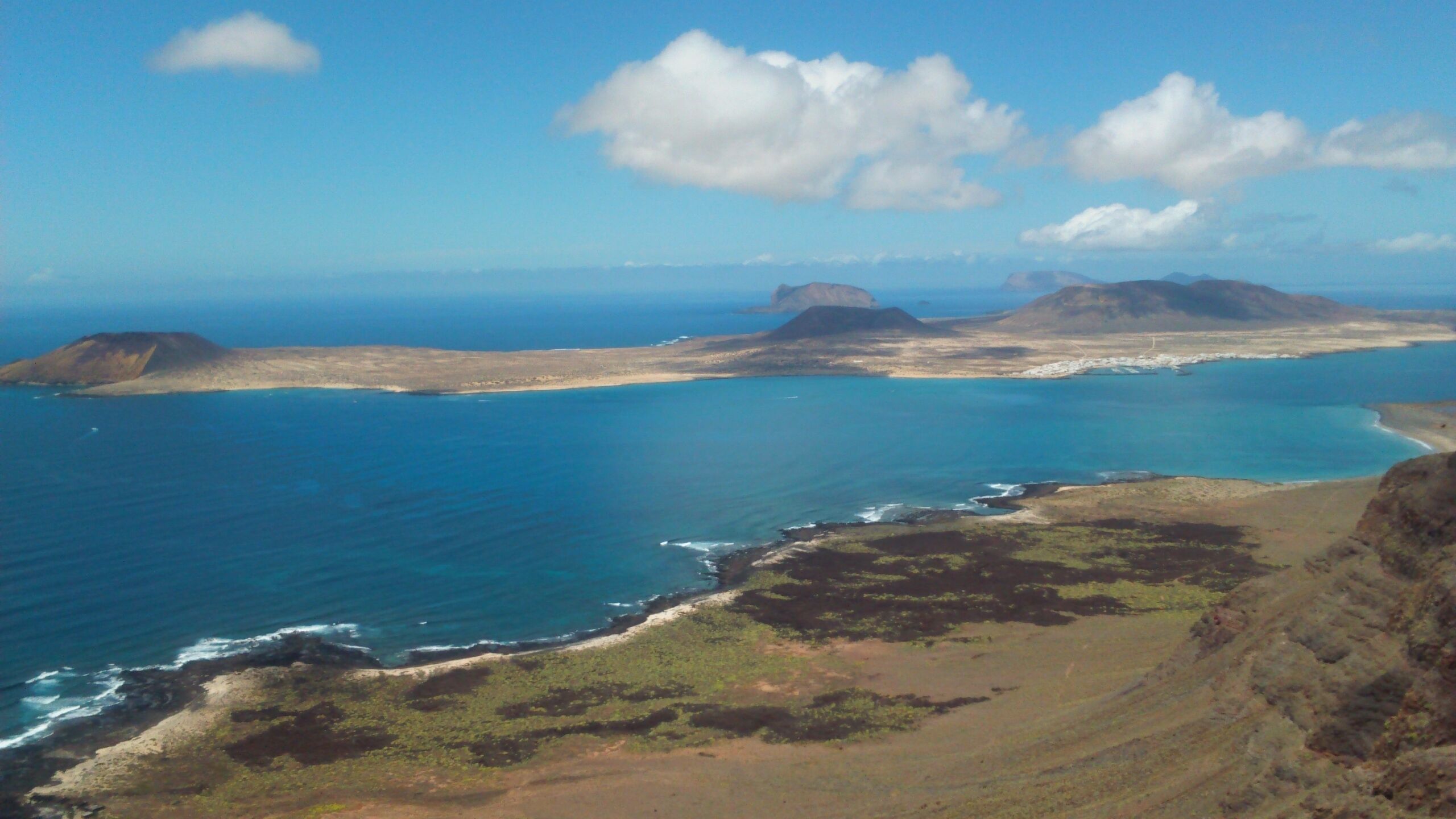 A coastal landscape with a clear sky, a large body of water, and distant mountains.