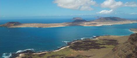 A coastal landscape with a clear sky, a large body of water, and distant mountains.