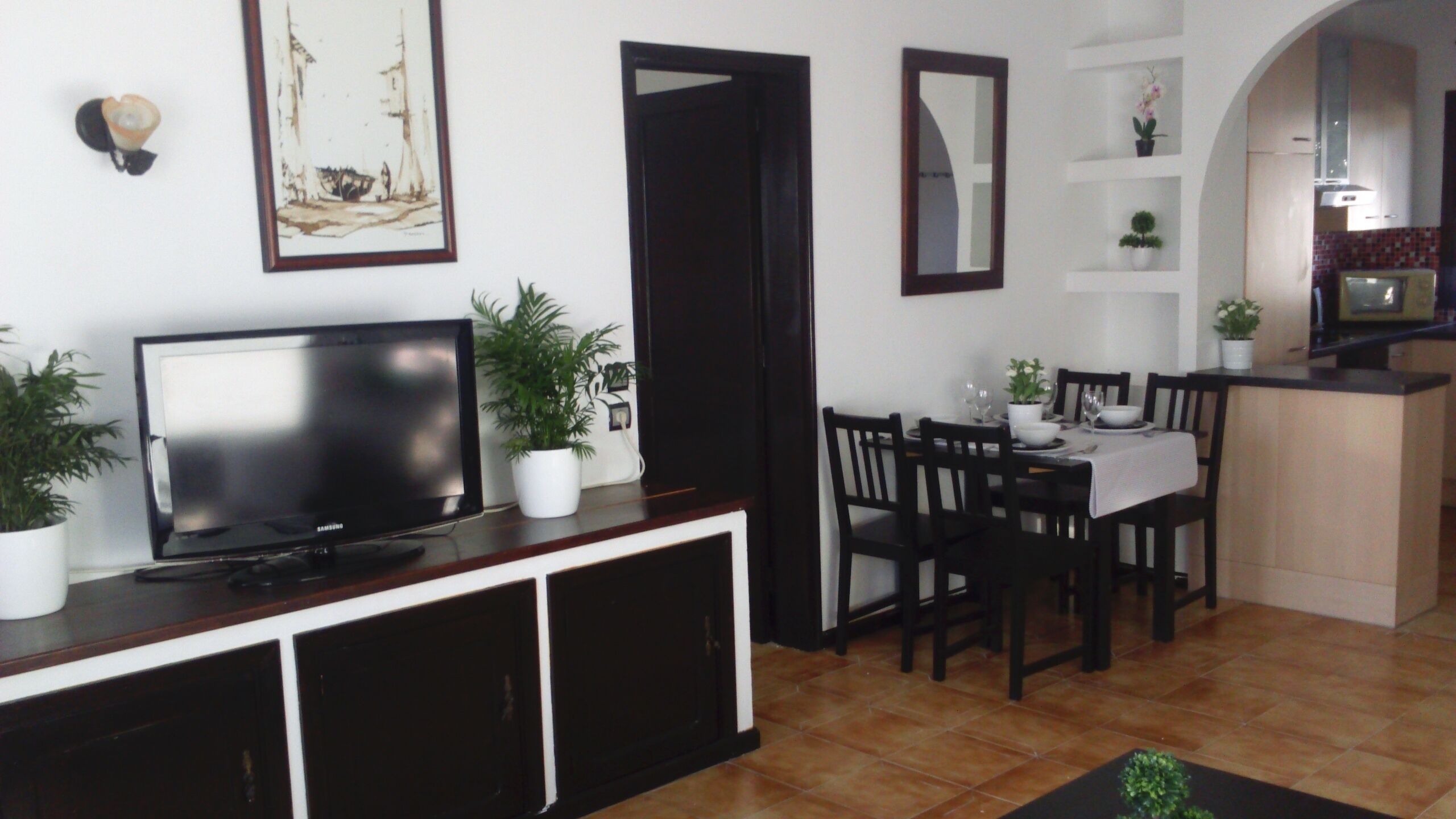 Ein Wohnzimmer mit Fernseher, Esstisch, Stühlen und Topfpflanzen.