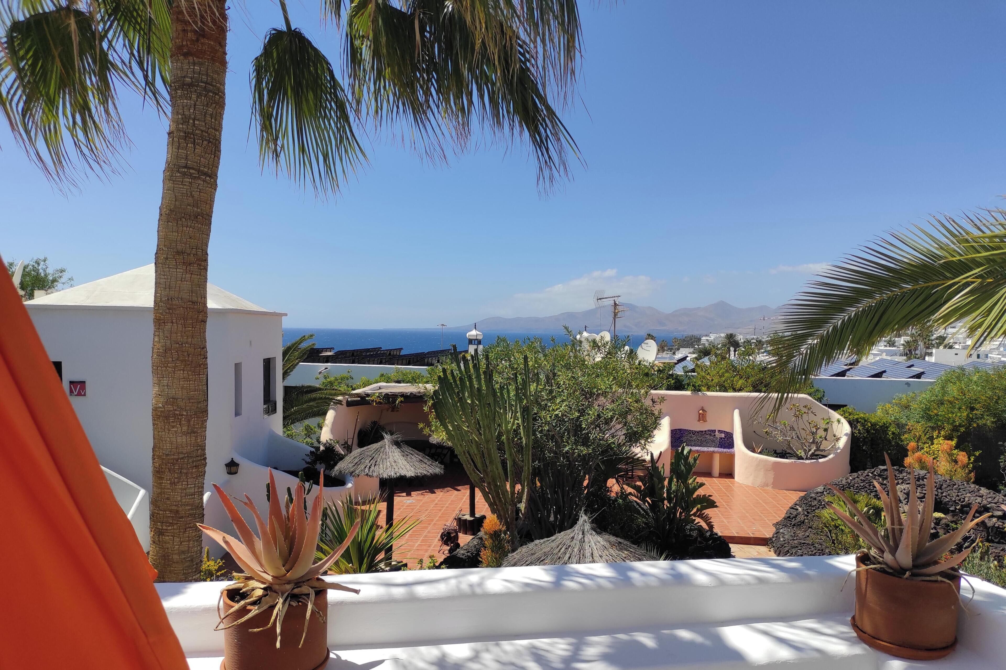 Una terraza con plantas en macetas, una pared blanca y vistas al mar y a las montañas.