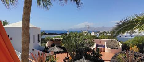 Una terraza con plantas en macetas, una pared blanca y vistas al mar y a las montañas.