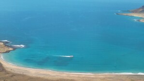 An aerial view of a coastal area with clear blue waters, a sandy beach, and a boat in the distance.
