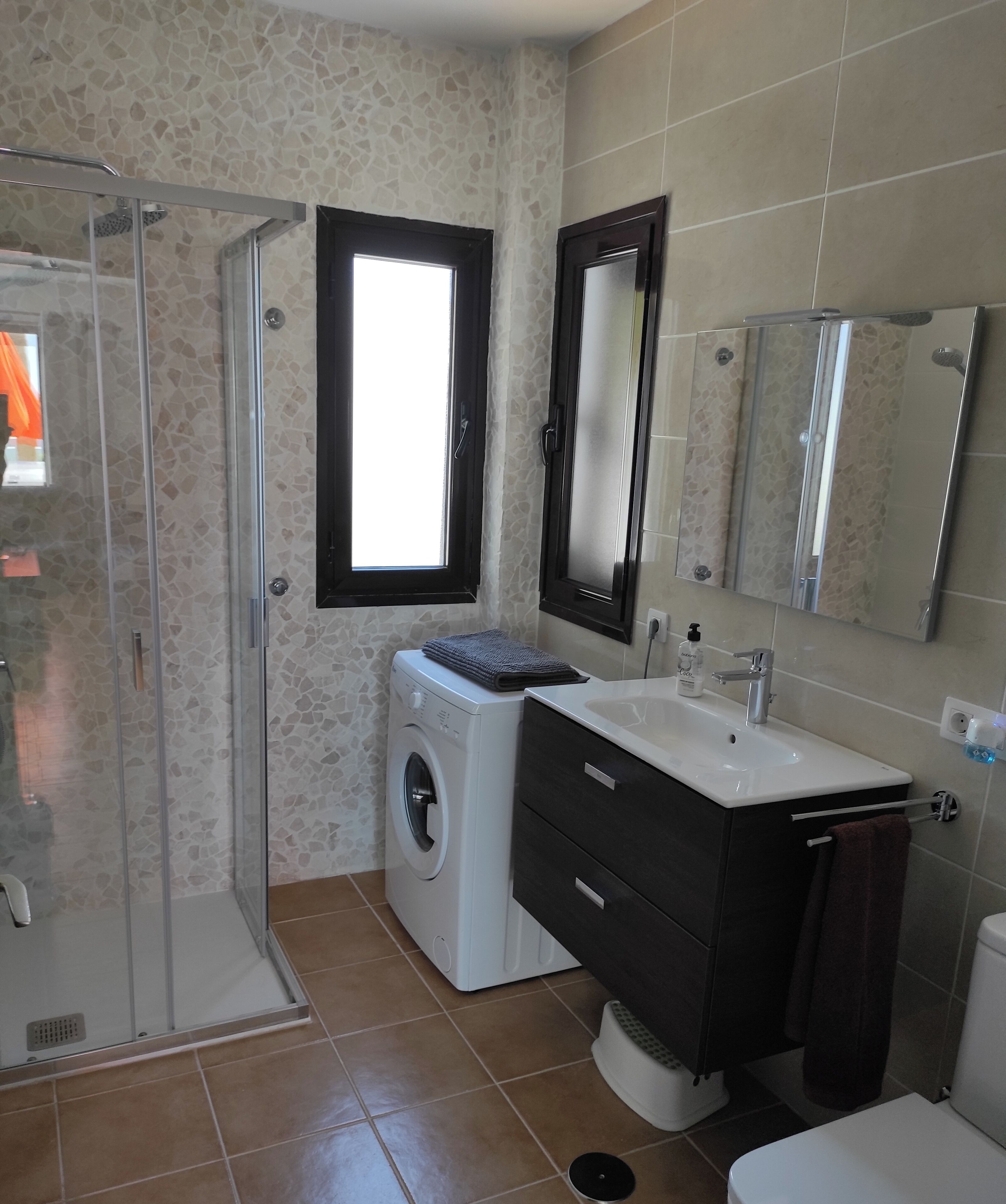 Un baño con cabina de ducha de vidrio, lavadora, lavabo con espejo e inodoro.