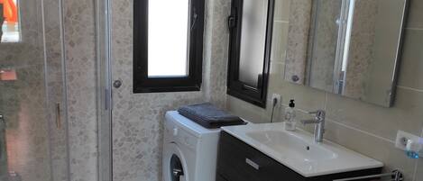 Un baño con cabina de ducha de vidrio, lavadora, lavabo con espejo e inodoro.