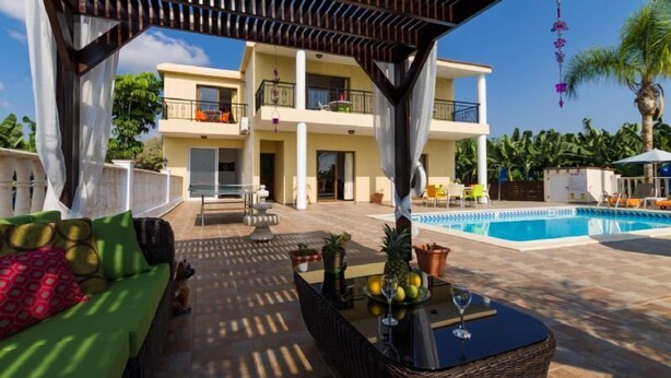 A covered outdoor area with a pool, wicker furniture, and a view of a two-story building. - 5 Bed, 5 Bath Villa with Private Pool in Affluent Residence of Sea Caves (Paphos)