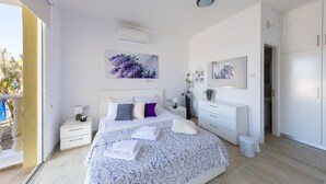 A modern bedroom with a large bed, white furniture, and artwork on the walls. - 5 Bed, 5 Bath Villa with Private Pool in Affluent Residence of Sea Caves (Paphos)