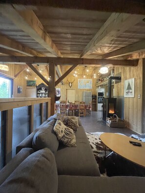 A cozy living room with a sofa, a coffee table, and a fireplace. There is a dining area with a table and chairs in the background. - Get back to basics in a chalet-style gîte for 6 to 15 people (Gérardmer)