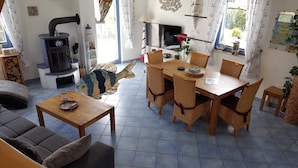 A cozy living room with a fireplace, a dining area with wicker chairs, and a sofa. - thatched roof house at the sea, pets welcome, fenced (Mecklemburg-Vorpommern)