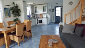 A spacious living room with a wooden coffee table, a grey sofa with cushions, and a dining area with wicker chairs and a wooden table. - thatched roof house at the sea, pets welcome, fenced (Mecklemburg-Vorpommern)