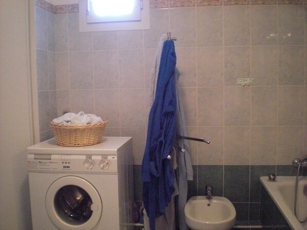 Une petite salle de bain équipée d’un lave-linge, d’un lavabo et d’une petite fenêtre.