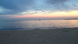 Uma praia com mar calmo e um veleiro ao longe.