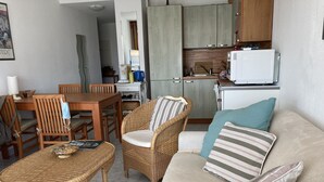 Um espaço de estar compacto com uma mesa de jantar, cadeiras de vime, um sofá com almofadas e uma área de cozinha compacta.