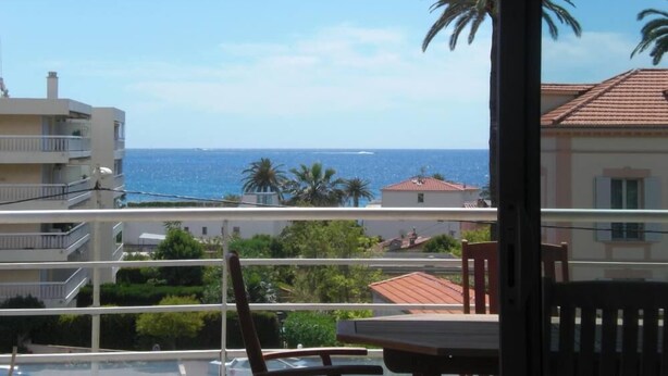 Varanda com vista para o mar e palmeiras, uma mesa e uma cadeira.