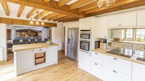 Eine moderne Küche mit Holzbalken, einer zentralen Kochinsel, weißen Schränken und Edelstahlgeräten.