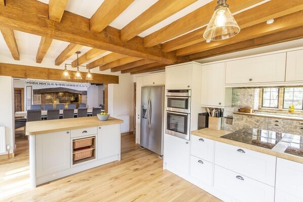 Une cuisine moderne avec des poutres en bois, un îlot central, des meubles blancs et des appareils électroménagers en acier inoxydable.
