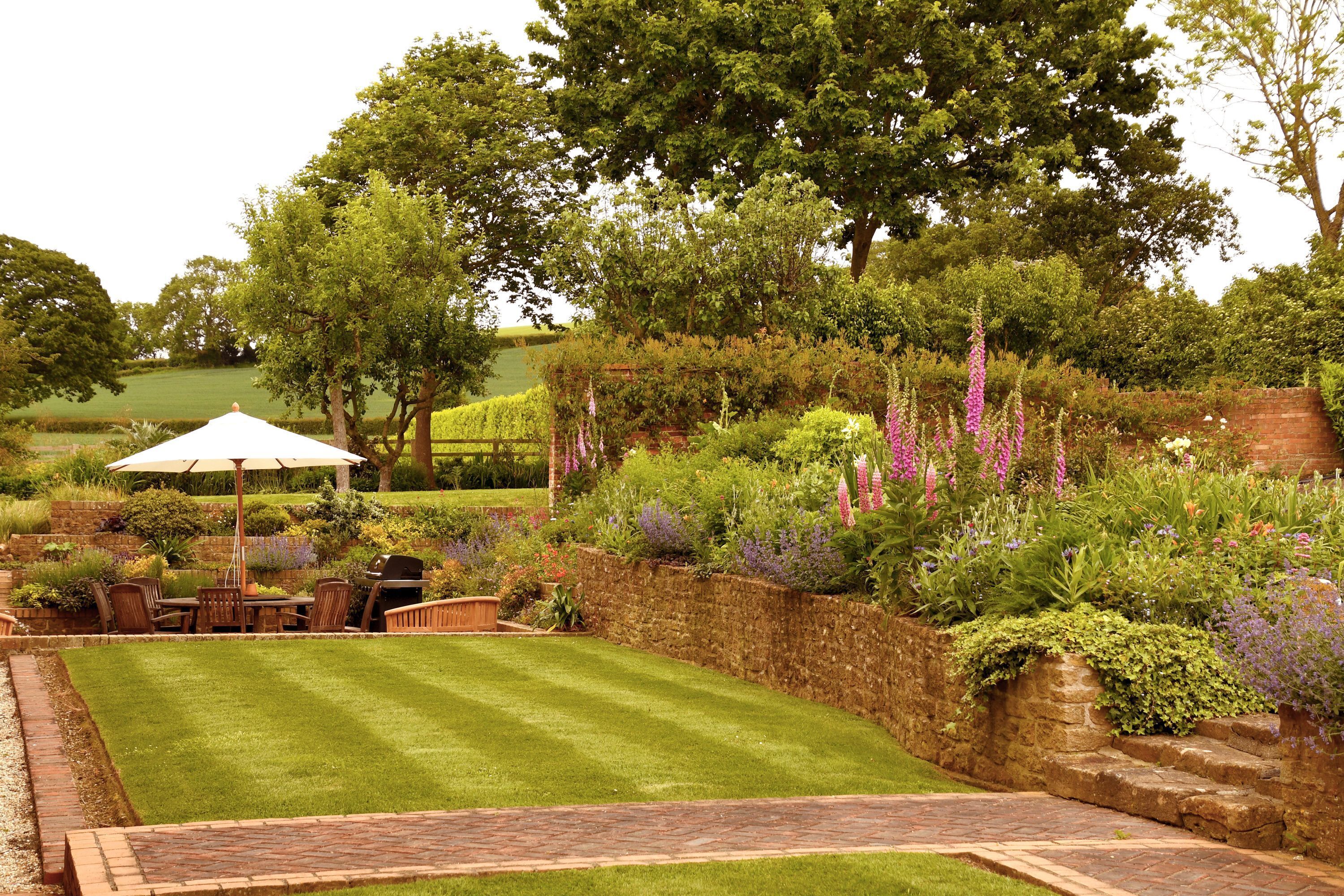 A well-maintained garden with a lawn, a brick patio, and a dining area with outdoor furniture.