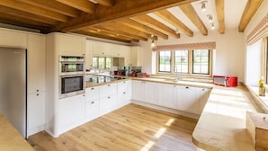 Eine geräumige Küche mit weißen Schränken, einer Holzbalkendecke und einem großen Fenster, das für natürliches Licht sorgt.