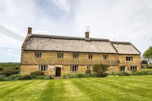 A stone farmhouse with a thatched roof, multiple windows, and a well-maintained lawn. - Historic Farmhouse with style (Martock)