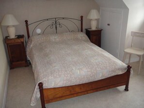 A bedroom with a wooden bed, two bedside tables with lamps, a chair, and a door.