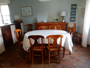 A dining area with a round table covered by a white tablecloth, surrounded by wooden chairs.
