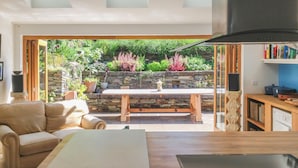 A modern living room with a sofa, a dining table, and a kitchen area visible through an open door. - Luxury House With Magnificent Sea Views (Tintagel)
