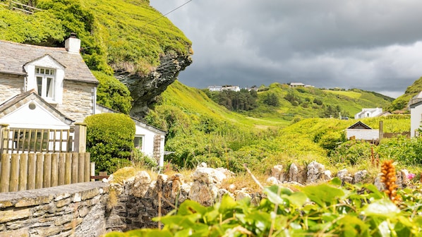 A coastal village with stone houses, lush greenery, and a cliff overlooking the sea.
