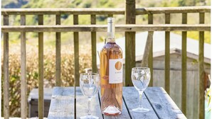 A bottle of L'OSTAL wine on a wooden table with two glasses, set against a scenic hillside backdrop. - Luxury House With Magnificent Sea Views (Tintagel)