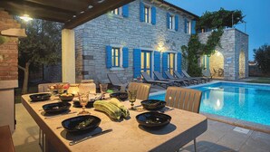 An outdoor dining area with a pool, stone building, and blue shutters. - Villa Nina in Vodnjan (Vodnjan)