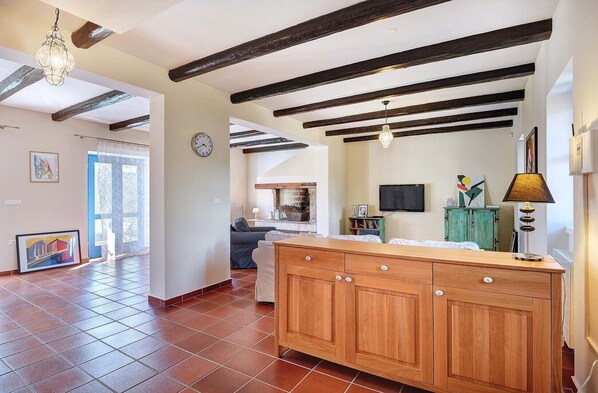 A spacious living area with exposed wooden beams, a fireplace, a dining area with a wooden table and cabinets, and a television on the wall. - Villa Nina in Vodnjan (Vodnjan)