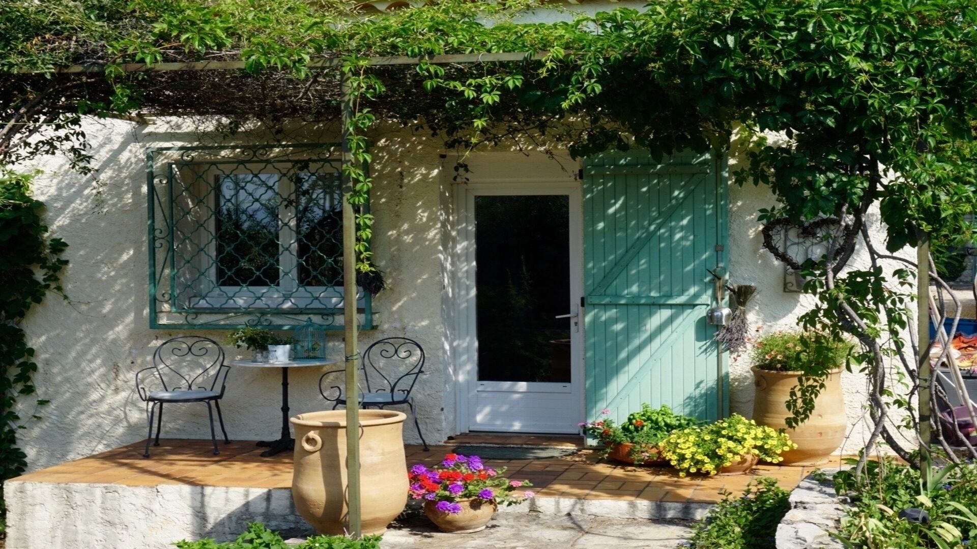 A quaint cottage with a small patio, a door, and a window with a metal grille.