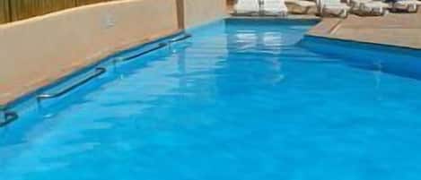 Una piscina azul cristalina con sillas de descanso y sombrillas.