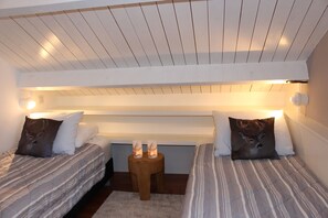 Un dormitorio con dos camas, cabeceros de madera, un taburete de madera pequeño con velas y un techo blanco.