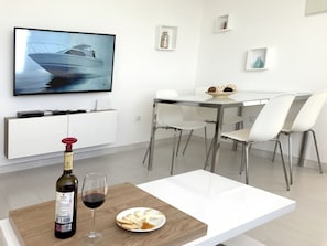 A modern dining area with a white table, chairs, and a television displaying a boat on the wall.