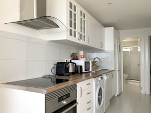 A modern kitchen with white cabinets, a stainless steel range hood, a built-in oven, a microwave, and a washing machine.