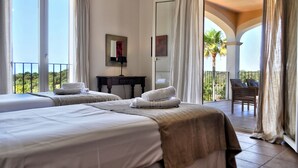 Camera d'albergo con due letti, una scrivania, una sedia e un balcone con vista su palme.