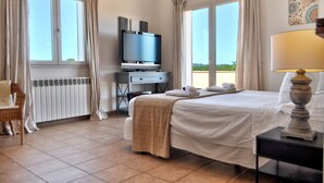 Una camera d'albergo con un letto, una scrivania con televisore, una sedia e vista sull'esterno.