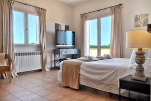 A hotel room with a bed, a desk with a television, a chair, and a view of the outdoors. - VILLA GATONA, our most popular luxury Villa - modern and impressive pool & Villa (Felanitx)