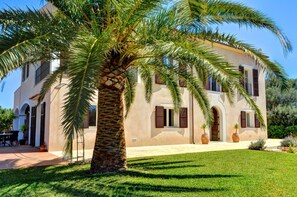 Un edificio de dos pisos con fachada de estuco, ventanas arqueadas y una palmera en primer plano.