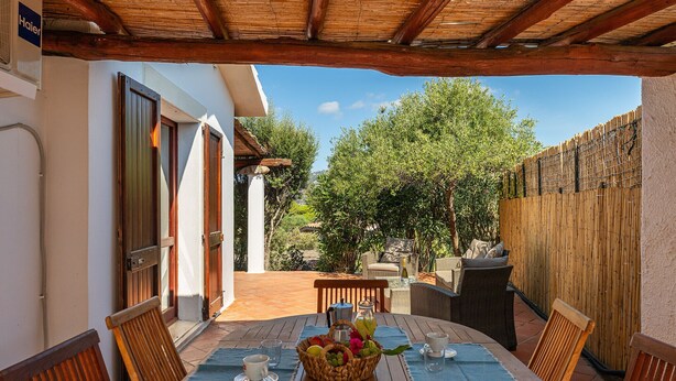 Eine Terrasse im Freien mit einem Holztisch, der zum Essen gedeckt ist, Korbstühlen und einem Korb voller Früchte.