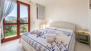 Ein Schlafzimmer mit Bett, Nachttisch, Lampe und Blick ins Freie.